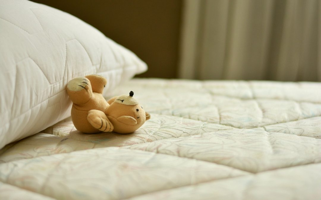 bare white mattress with a teddy bear near a pillow on the left side of the image